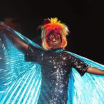 Ebony Rose Dark - Profile picture. A black drag queen with rainbow hair and blue angel wings.